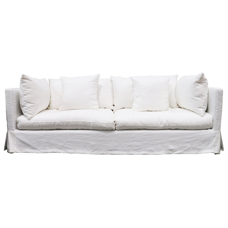 White slipcovered three-seat sofa with loose back cushions and a skirted base, on a white background