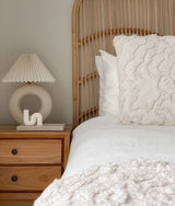 A white bed with a rattan headboard and nightstand, featuring Bengali Collections' IVORY TUFTED CUSHION COVER.