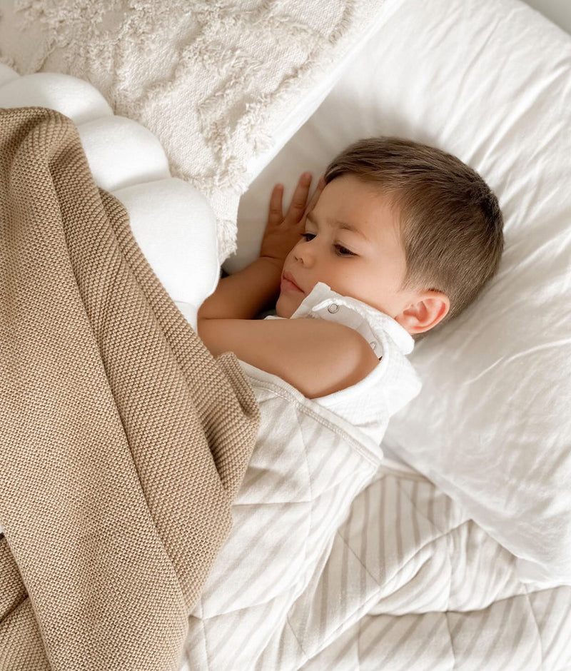 A baby peacefully sleeping on a Bengali Collections IVORY TUFTED CUSHION COVER bed with a blanket.