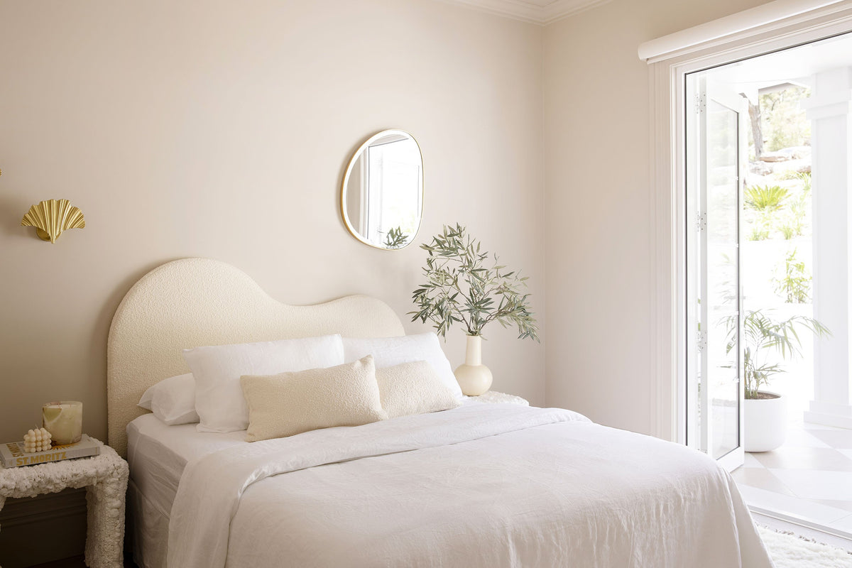 Soft neutral bedroom with a curved bedhead and a round mirror