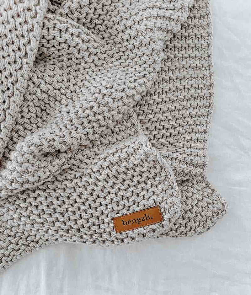 A Bengali Collections CHUNKY KNIT OATMEAL THROW on a white bed.