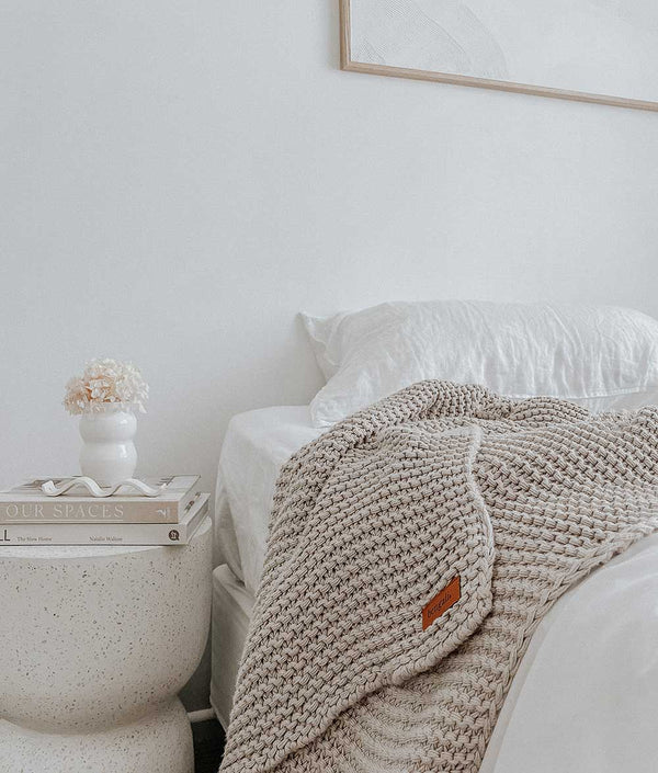 A white bed with a CHUNKY KNIT OATMEAL THROW by Bengali Collections on it, made of pure cotton.