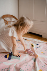 A little girl engaging with Raindrops Village - Interactive toy from the Play Pouch range on a pink rug.