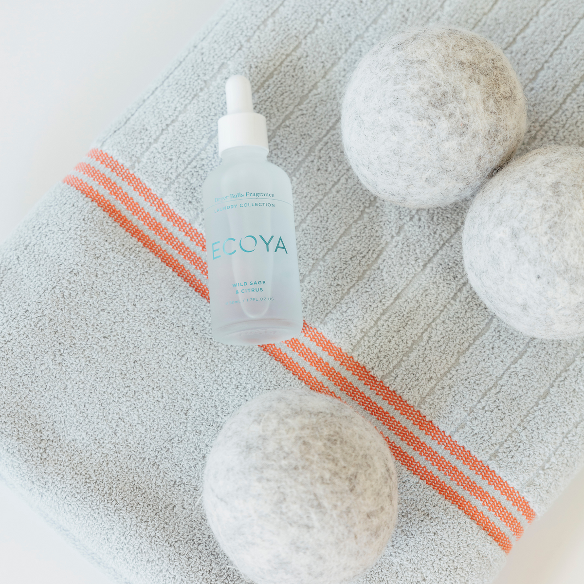 Ecoya fragrance dropper and wool dryer balls laid on a grey towel with orange stripes