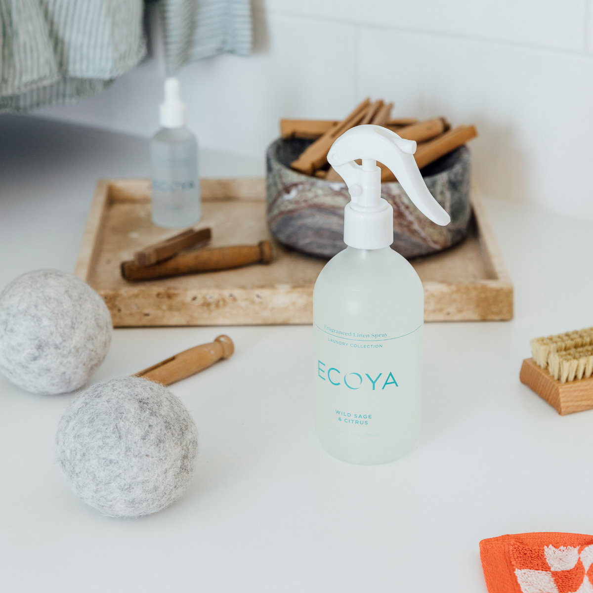 Ecoya linen spray and wool dryer balls on a laundry bench with a wooden tray and brush