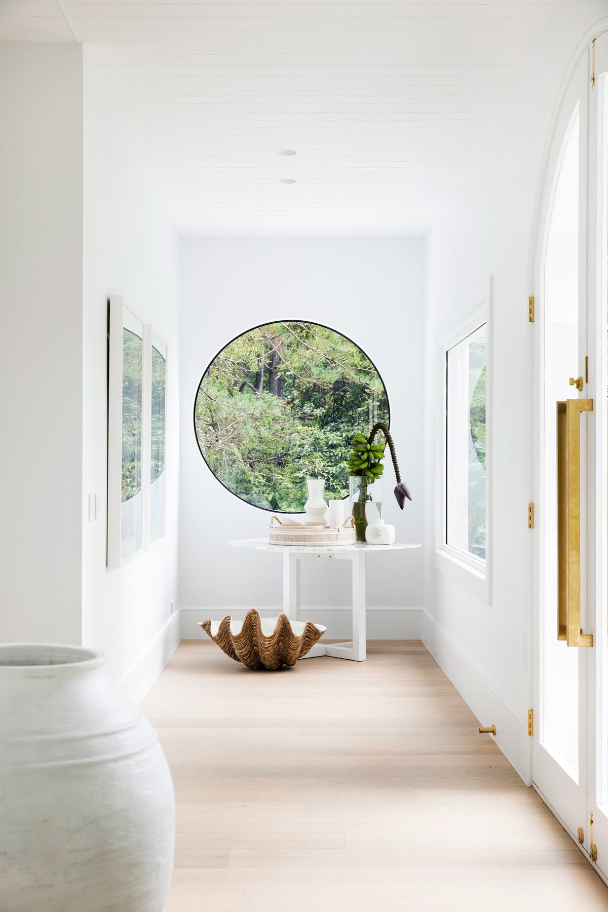 White hallway ending in a round garden window above a console