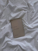 A Beauty in the Stillness book laying on a bed with white sheets by Thought Catalog.