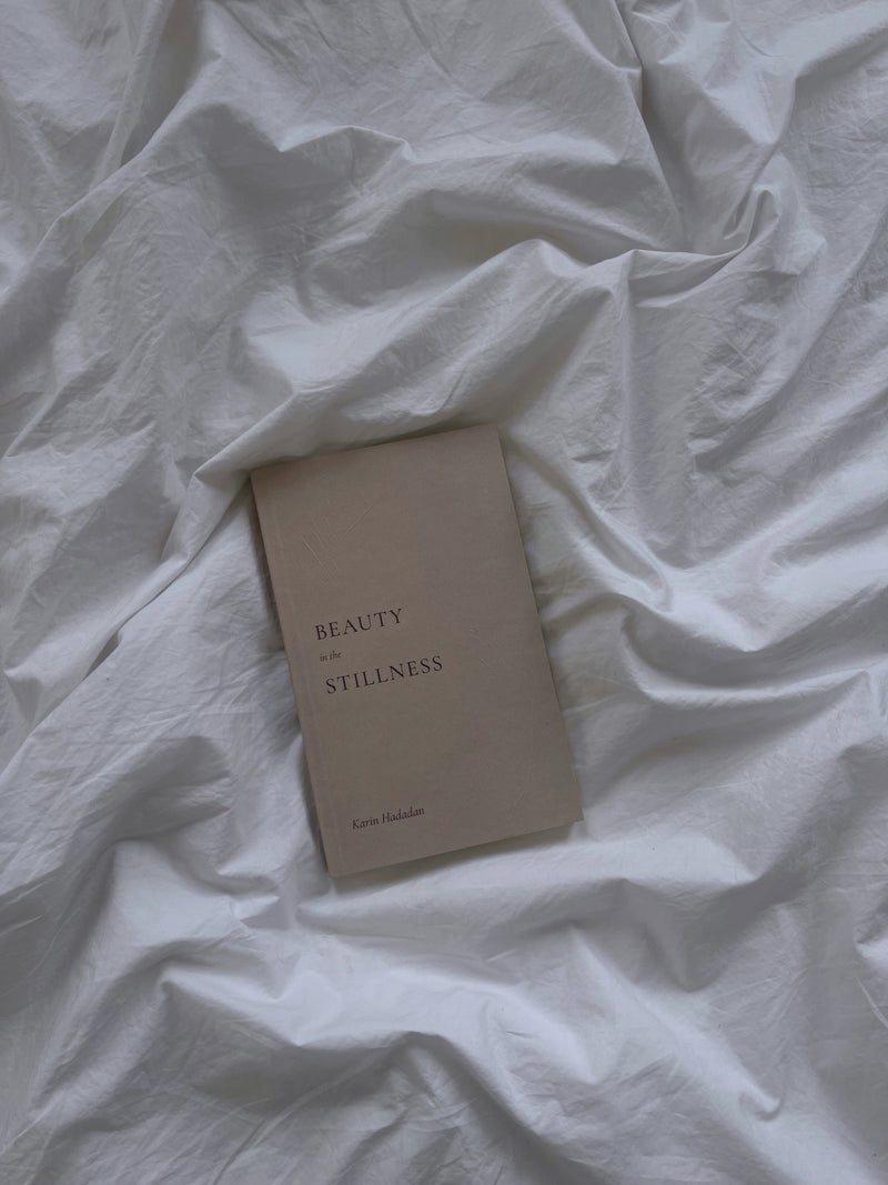 A Beauty in the Stillness book laying on a bed with white sheets by Thought Catalog.