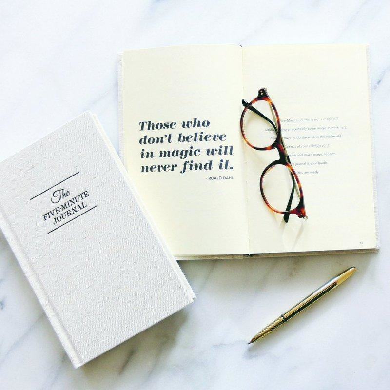 Five Minute Journal closed beside an open quote page and a pair of glasses