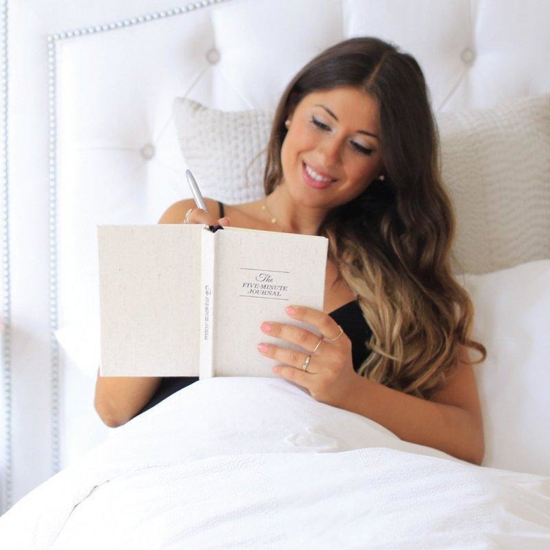 Woman writing in the Five Minute Journal while sitting up in bed