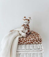 A GIRAFFE SNUGGLY from Bengali Collections sits on top of a wicker basket.