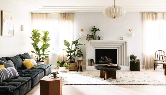 Spread from the book showing a white living room with a fireplace, dark sofa and tall pot plants