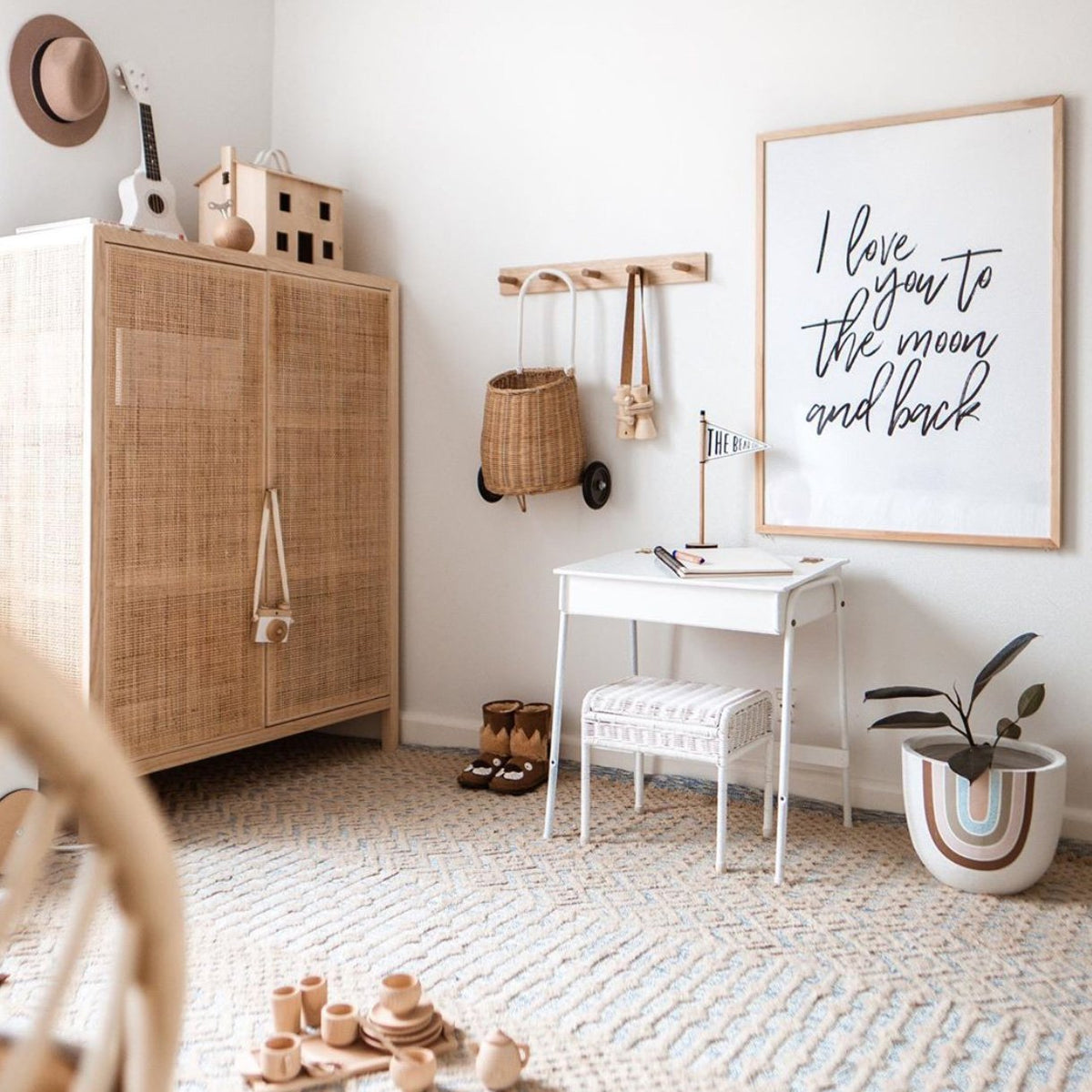 I Love You To The Moon print in a natural timber frame above a white desk in a nursery with a rattan cabinet