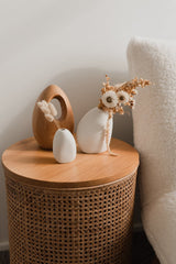 The Great Harmie Vase - White / Natural, handmade by Vietnamese artisans, adorns a wicker side table in the Ned Collections.