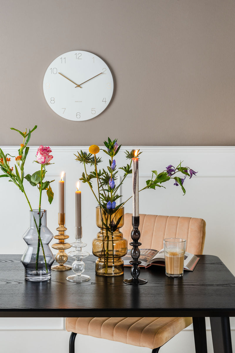 A table with candles, flowers and a Charm Wall Clock - Various Colours by Karlsson on the wall.