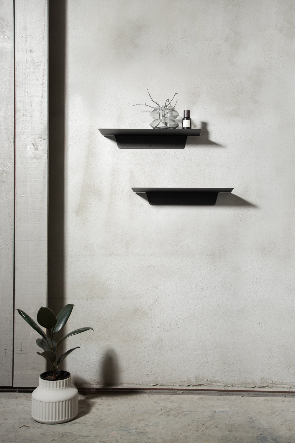 Two black FOLD Ledges on a concrete wall above a potted rubber plant