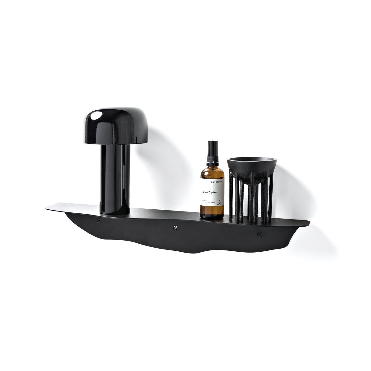 Black wavy shelf holding a cordless table lamp, a small amber bottle and a ribbed candle vessel