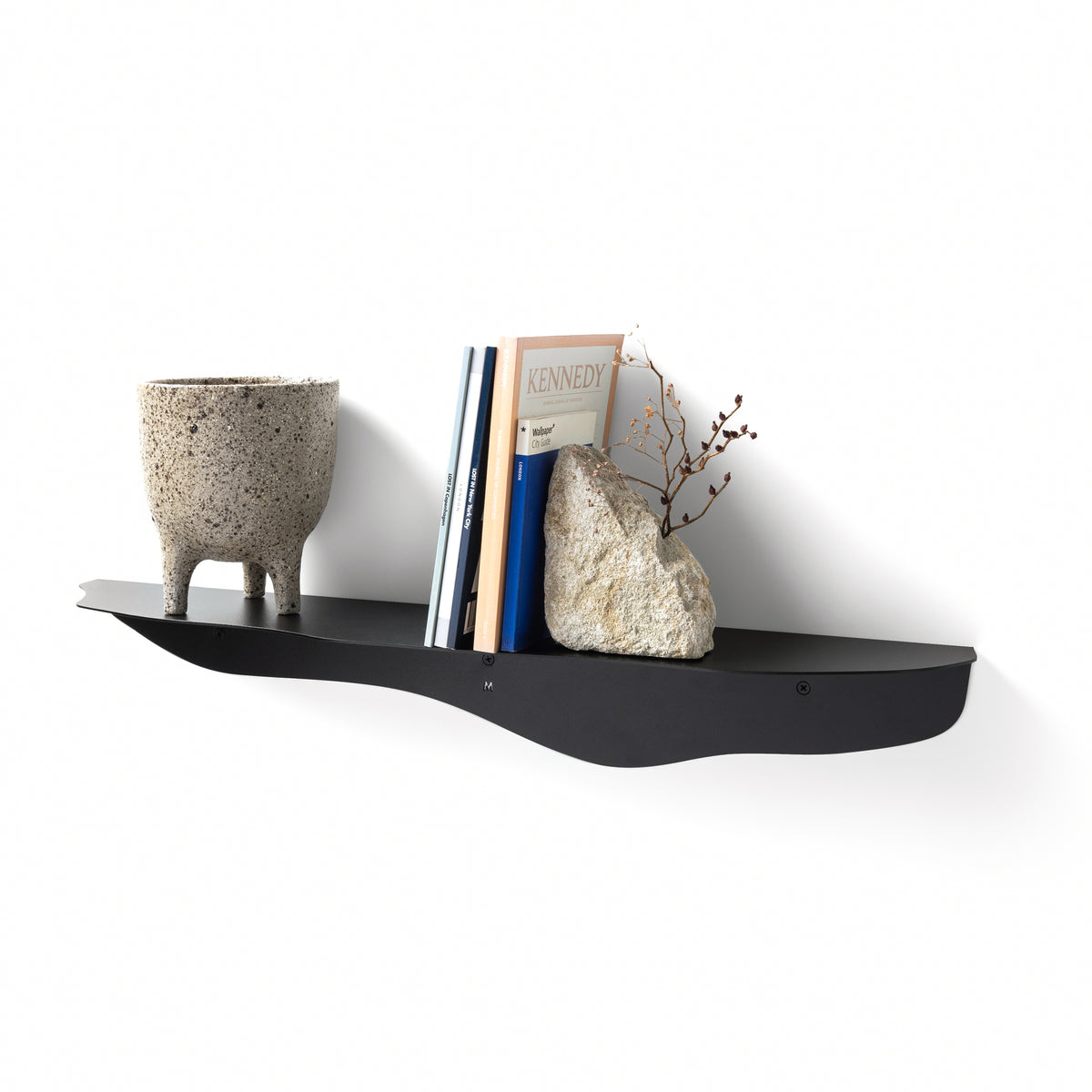 Black wavy shelf holding a footed stone planter, upright books and a pale stone vase of dried stems