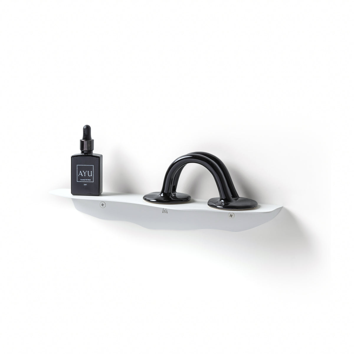 White wavy shelf on a white wall at an angle, holding a small dark bottle and a looped sculpture