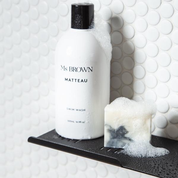 Black FOLD shower shelf with a white bottle and soap bar against white hex tiles