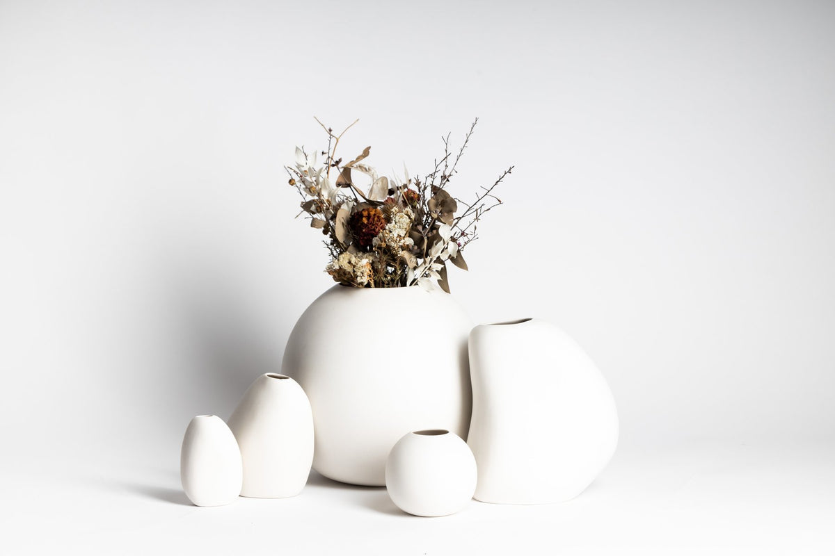 Group of white Harmie vases in different shapes, one holding dried flowers