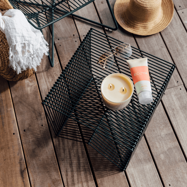 A Limited Edition Citronella & Lemongrass Outdoor Candle by Ecoya, sunglasses, and a bottle of water elegantly displayed on a table.