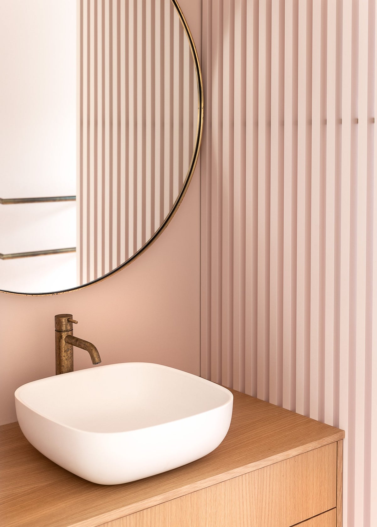 A bathroom with a white sink and a round mirror from Our Spaces - Contemporary New Zealand Interiors by Books.