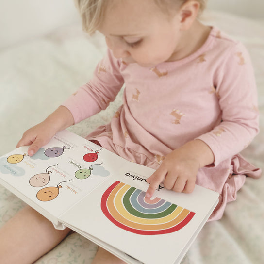 Toddler in pink reading the picture dictionary open at a rainbow page