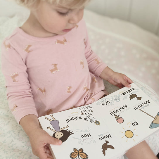 A little girl is reading a book with the MY FIRST TE REO MĀORI PICTURE DICTIONARY by As We Are Illustration.
