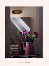 A book of pink tulips sits on a table in front of a window, bringing a touch of Home | Victoria Alexander to the space.