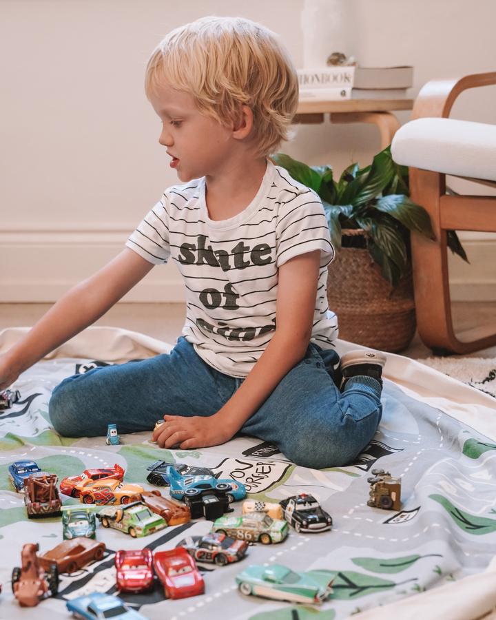 A young boy engaging in imaginative play with Wow Town Track Interactive toy cars on a rug. Brand Name: Play Pouch