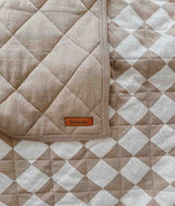 A beige and white REVERSIBLE QUILT - KHAKI GINGHAM blanket on a bed by Bengali Collections.