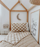 A bed with a wooden frame and a REVERSIBLE QUILT - KHAKI GINGHAM blanket by Bengali Collections.