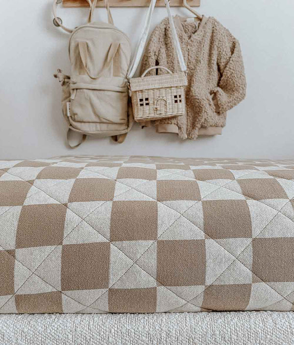 A bed with a REVERSIBLE QUILT - KHAKI GINGHAM by Bengali Collections and a backpack hanging on the wall.