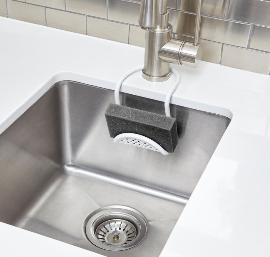 Umbra Sling sink caddy in white holding a dark sponge over a stainless steel sink