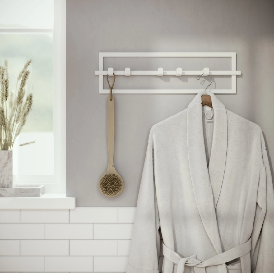 Umbra Cubiko 5 hook wall rack in white in a bathroom, holding a robe and a wooden brush