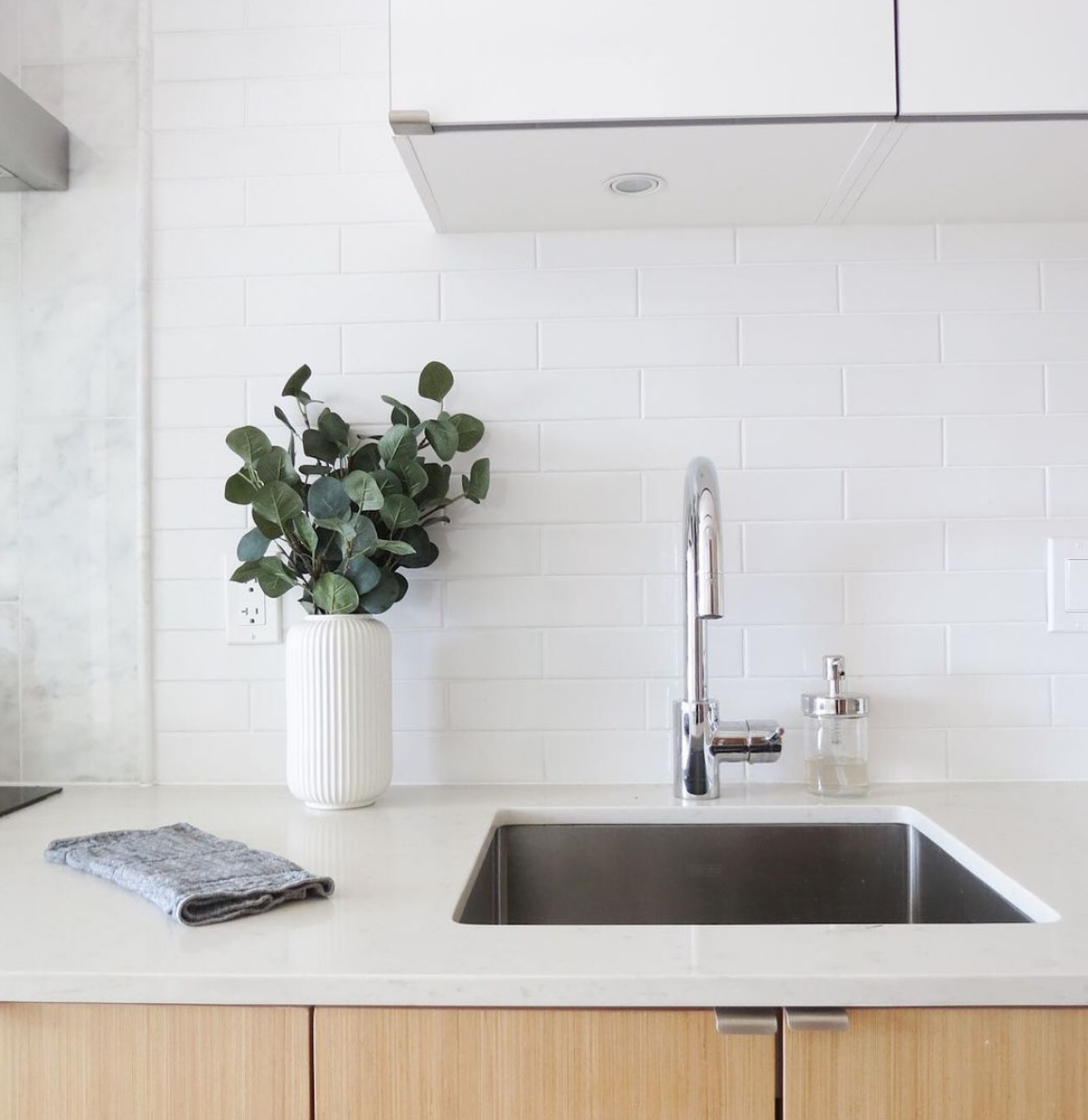 Grey dishcloth folded beside the sink in a white kitchen with a vase of eucalyptus