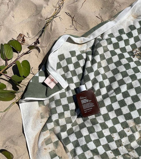 A beach towel with a bottle of We Are Feel Good Inc. Coconut Sunscreen SPF 50+ on it.