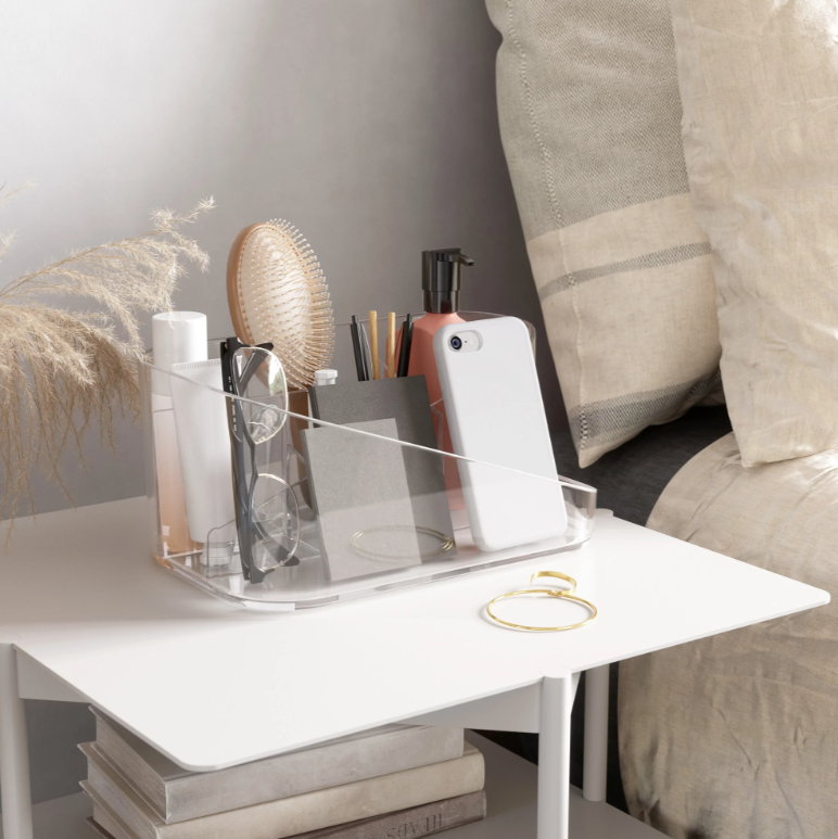 Umbra Glam clear organiser on a bedside table holding makeup and a mirror