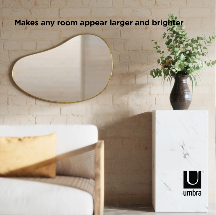 Umbra Hubba Pebble Mirror with a metallic frame styled on a living room wall.