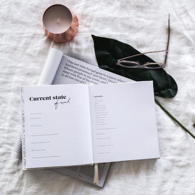 Press Pause open at a current state of mind page beside a pink candle and reading glasses
