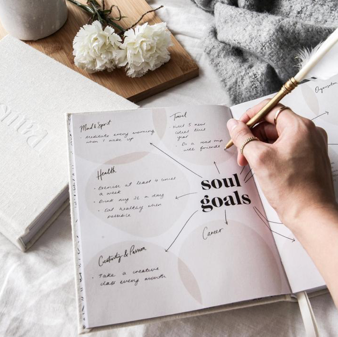 Hand writing in the Press Pause journal, open at a soul goals page