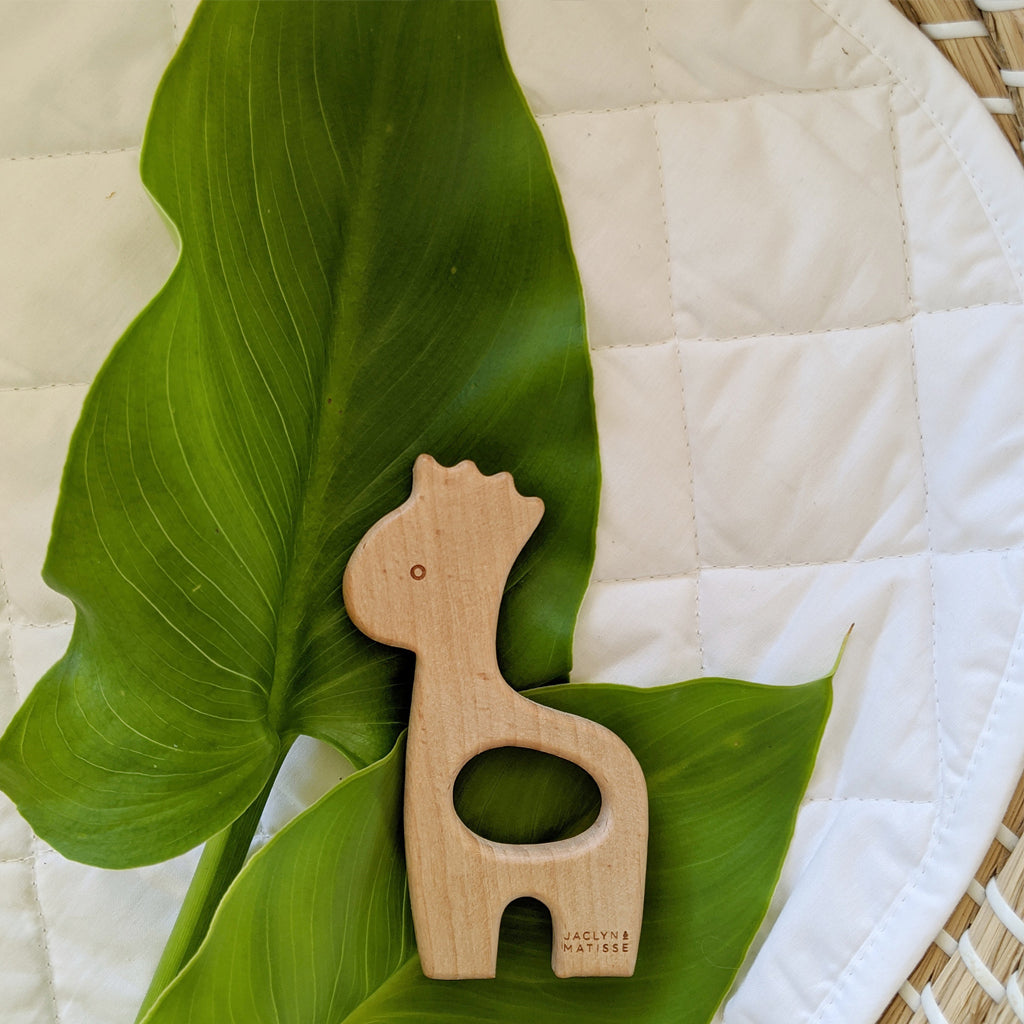 Wooden giraffe teether resting on a quilted mat beside a large green leaf