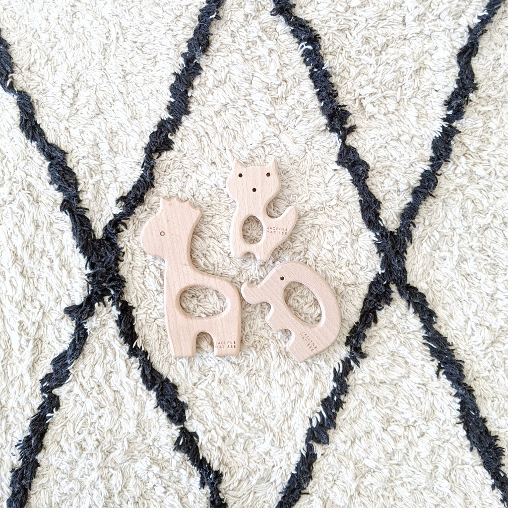 Wooden giraffe teether on a patterned rug beside a pink teether