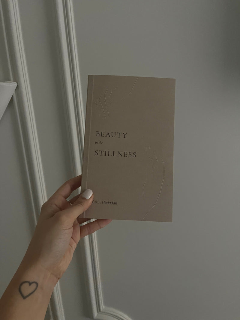 A person holding a book that says "Beauty in the Stillness" by Thought Catalog.