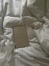 Beauty in the Stillness book by Thought Catalog laying on a bed with white sheets.