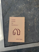 A book titled "Come Home to Yourself | Déjà Rae" by Thought Catalog that explores solitude and relationships, displayed on a sleek marble table.