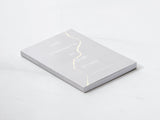A "The Strength In Our Scars | Bianca Sparacino" book with a gold foil cover on a white surface.