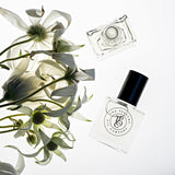 A bottle of MYTH perfume, inspired by Si (Giorgio Armani), next to a bunch of white flowers. (Brand Name: The Perfume Oil Company)