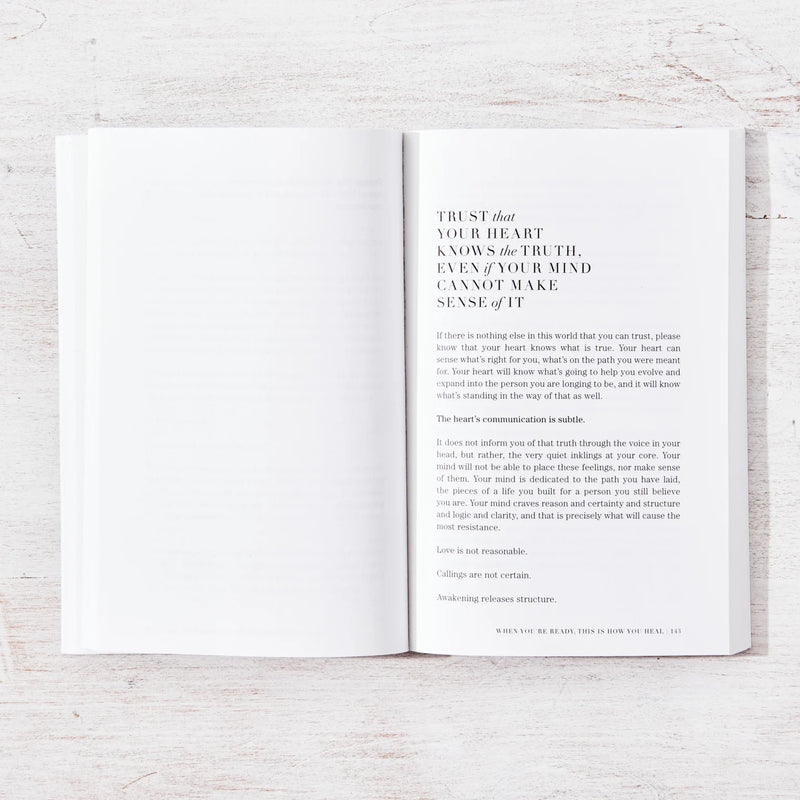 An open book, "When You're Ready, This Is How You Heal" by Brianna Wiest, providing inspiration and motivation for psychological healing, with a white cover on a wooden table.